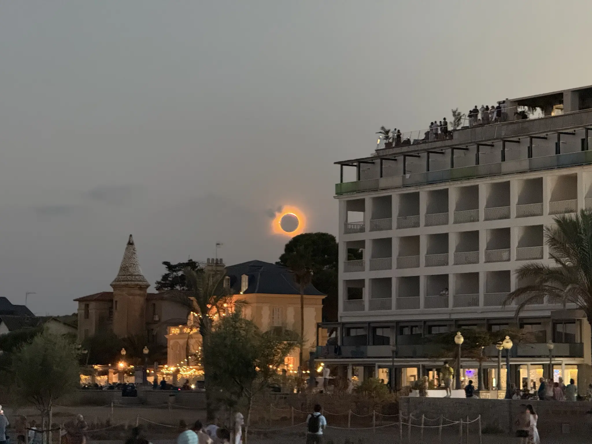 Eclipse total con un poco de nubosidad y a su lado hay un bloque de piso y una torre.