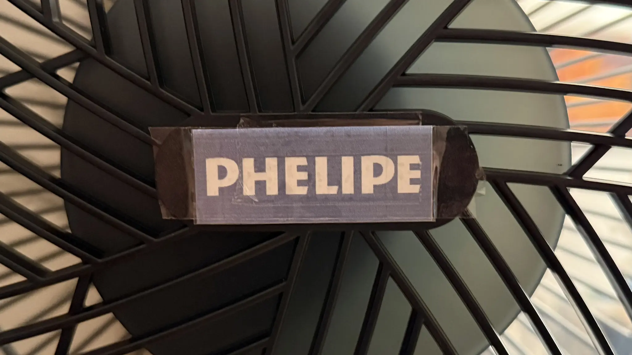 Frontal de un ventilador negro y donde hay el logotipo está superpuesto un trozo de papel pegado con cinta adhesiva con el logotipo de Philips editado como “PHELIPE”.