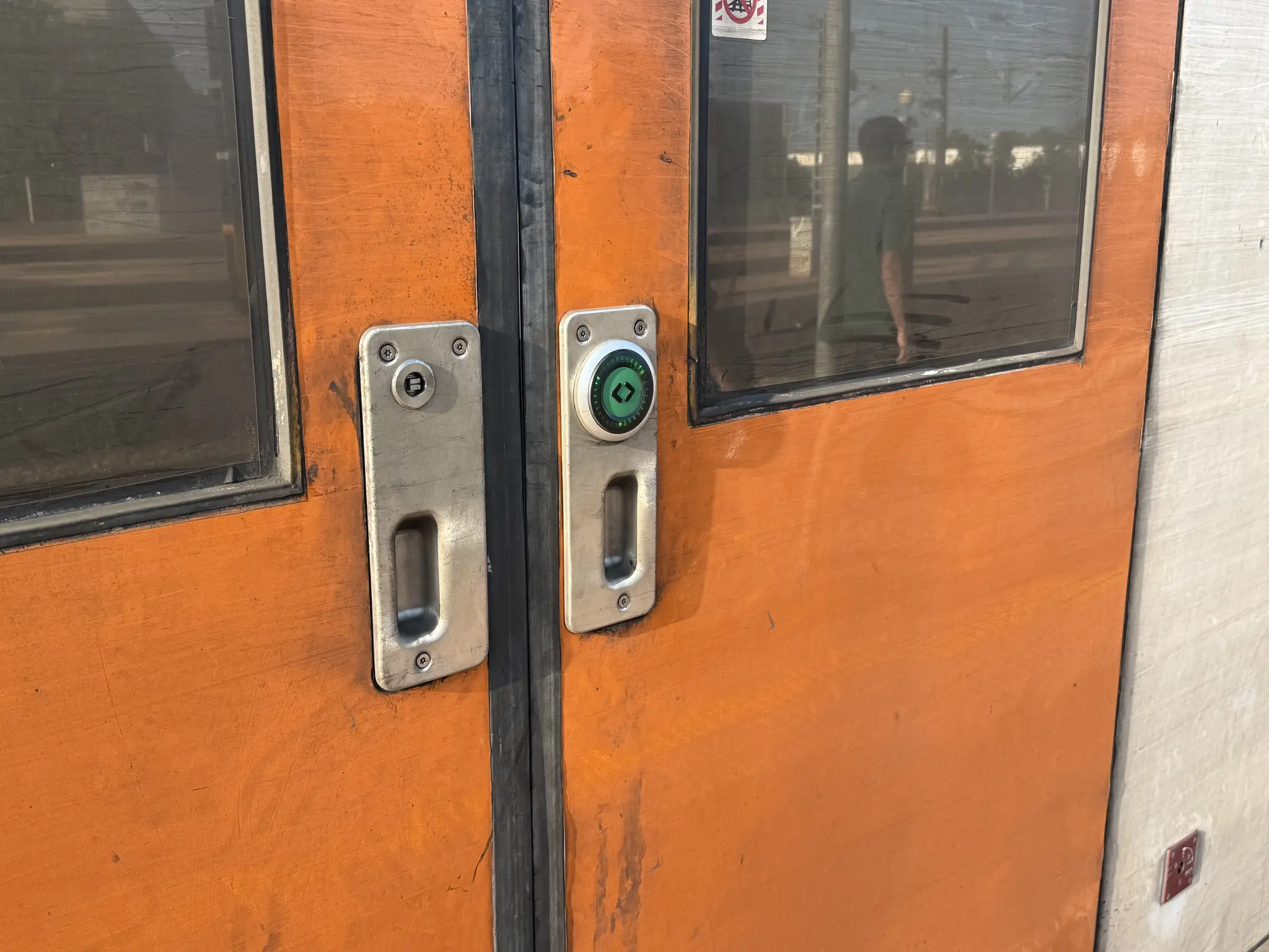 Porta de doble fulla taronja d’un tren de la sèrie 451, on es centra a la botonera, formada per dues xapes metàl·liques amb una maneta per obrir-les d’emergència amb el desbloqueig. La de la dreta conté un botó de color verd amb la vora ill·luminada de color verd.